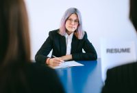 A young woman with dyed hair takes notes during a job interview.